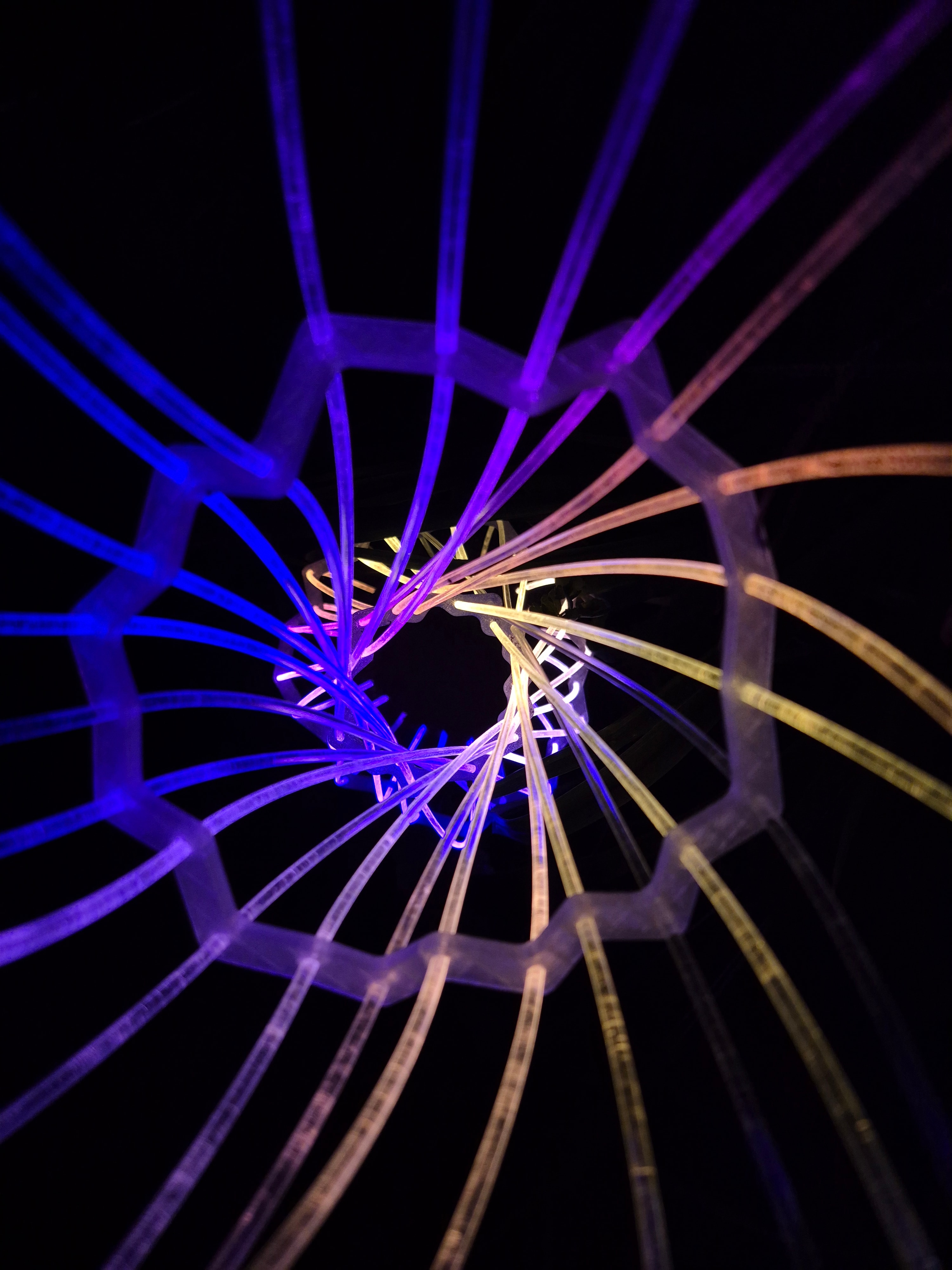 Fiberina — spiral vortex of blue and orange glowing rods seen from below