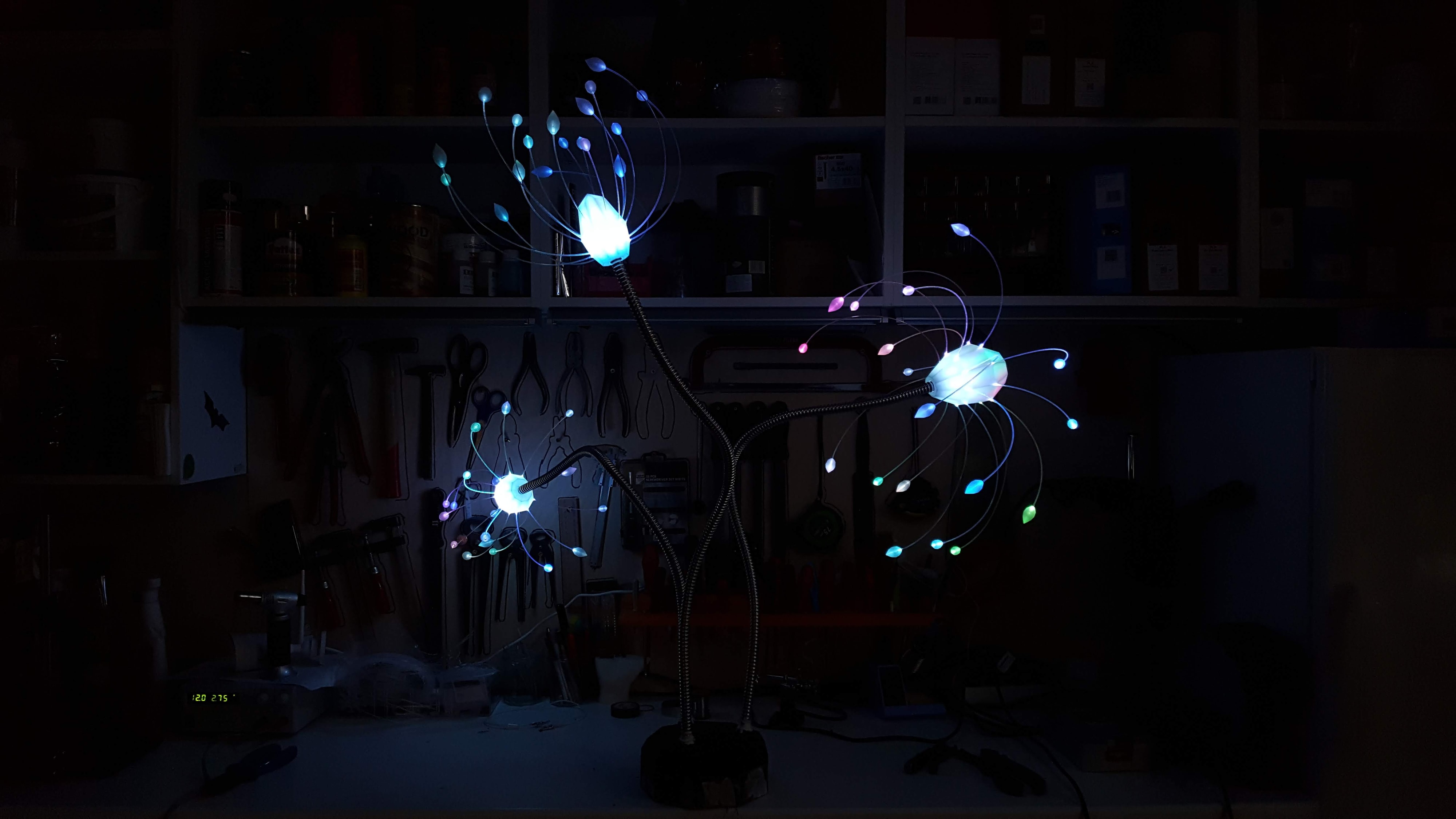 Tris — three-branch glowing flower lamp in cyan, pink, and white in a workshop