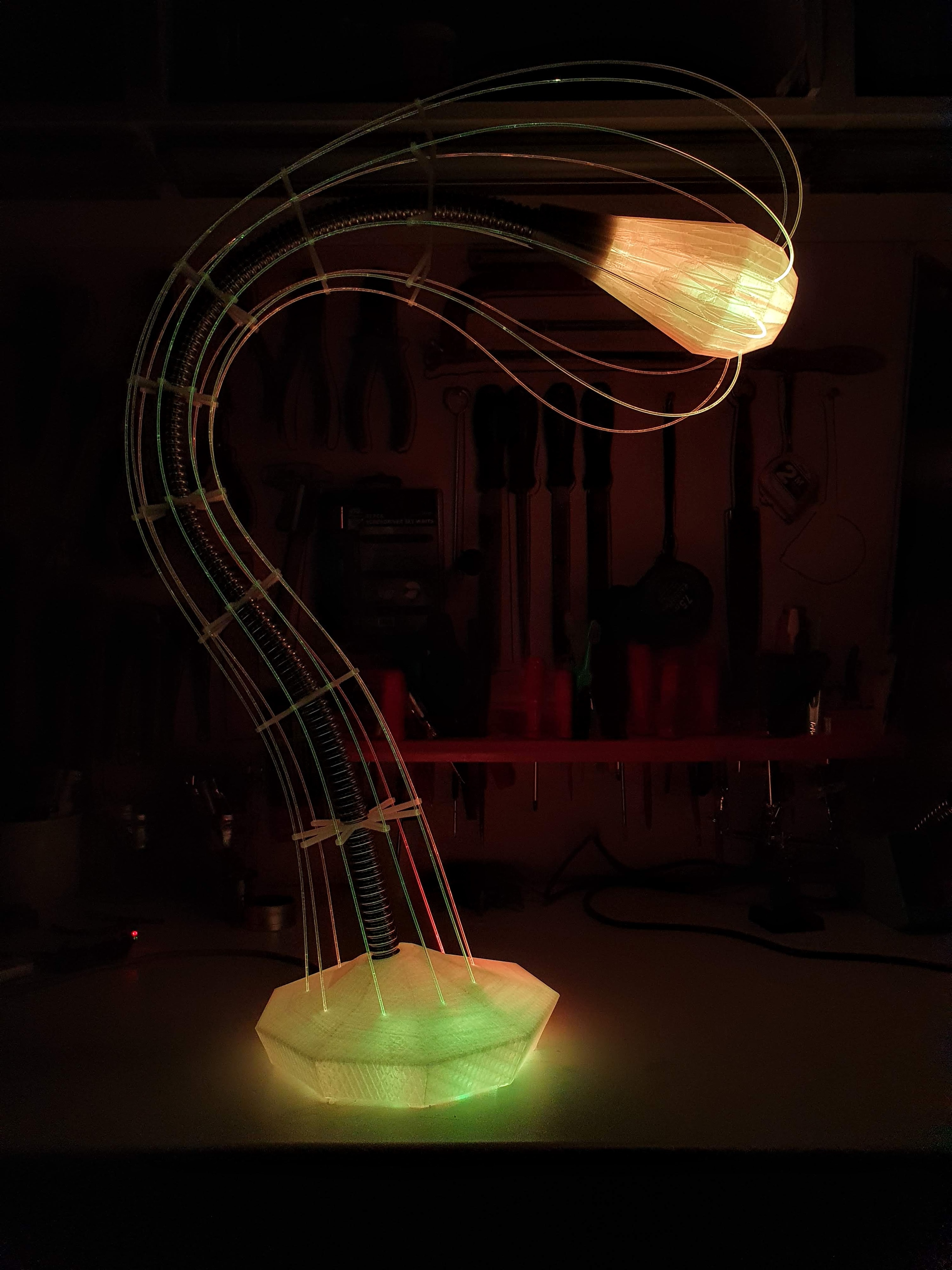 IXFID — 3D-printed curved lamp with green base and orange head in a dark workshop